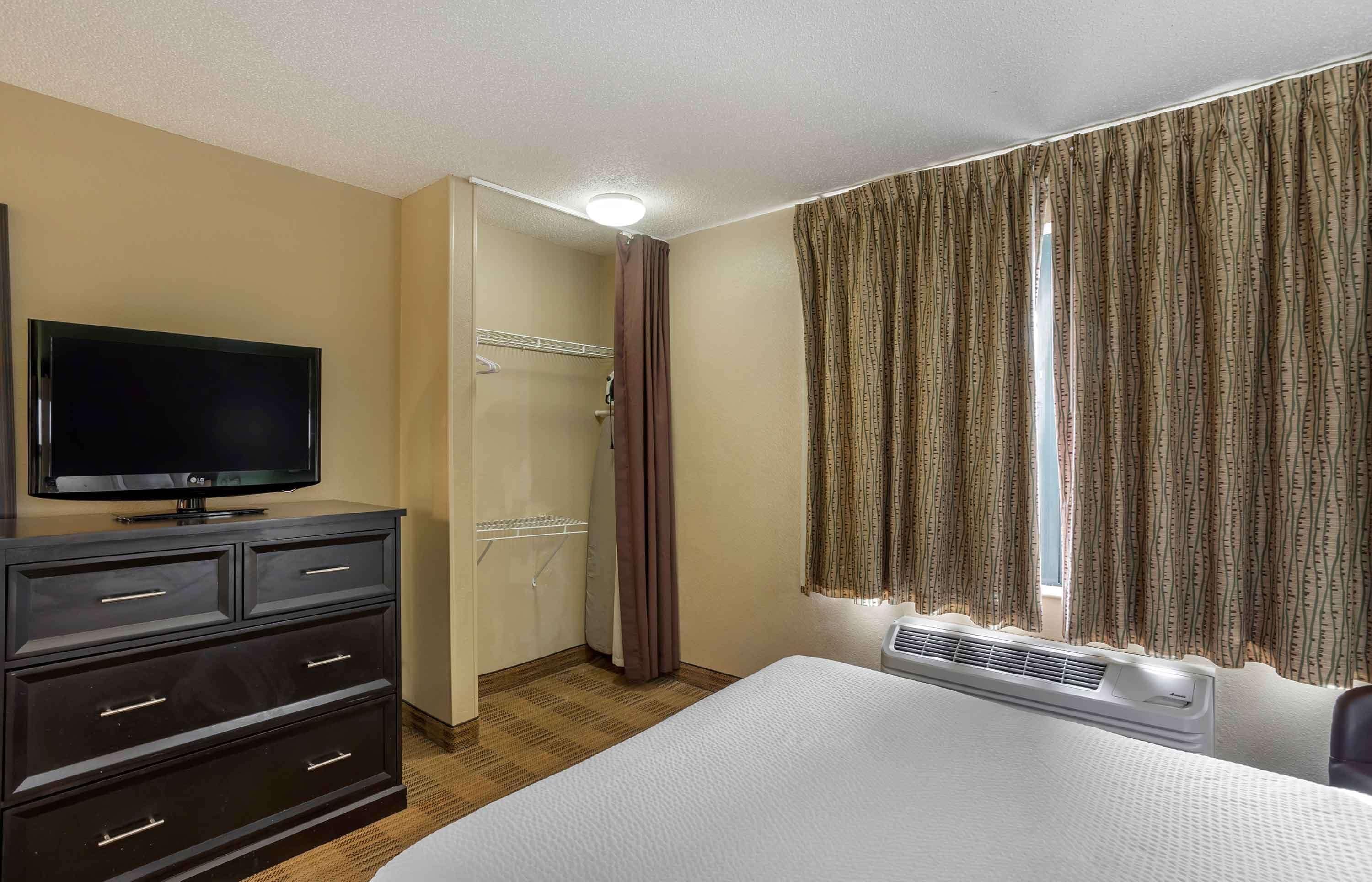 Ein Hotelzimmer mit Bett, Fernseher auf einer Kommode, Dusche und Vorhängen.