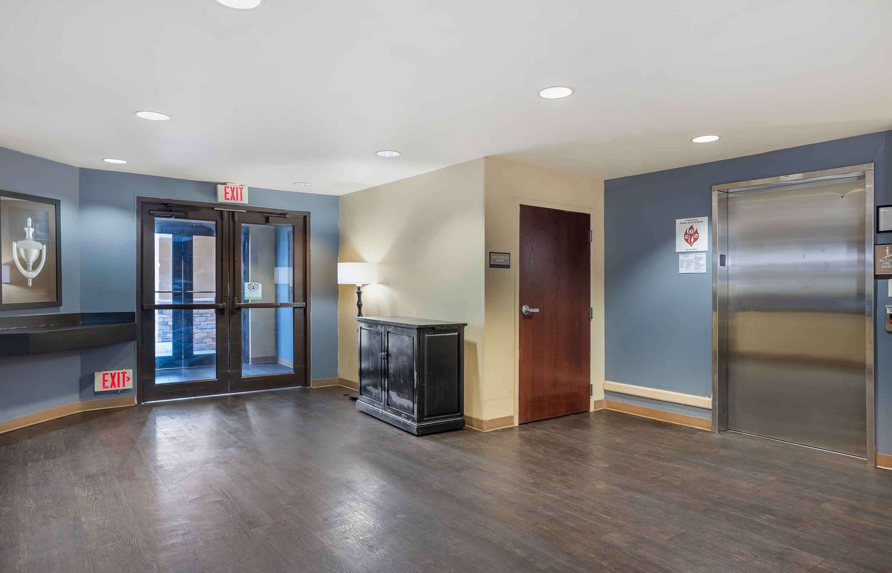 A hotel lobby with an exit sign, a reception desk, a wooden cabinet, a door, and a lift.
