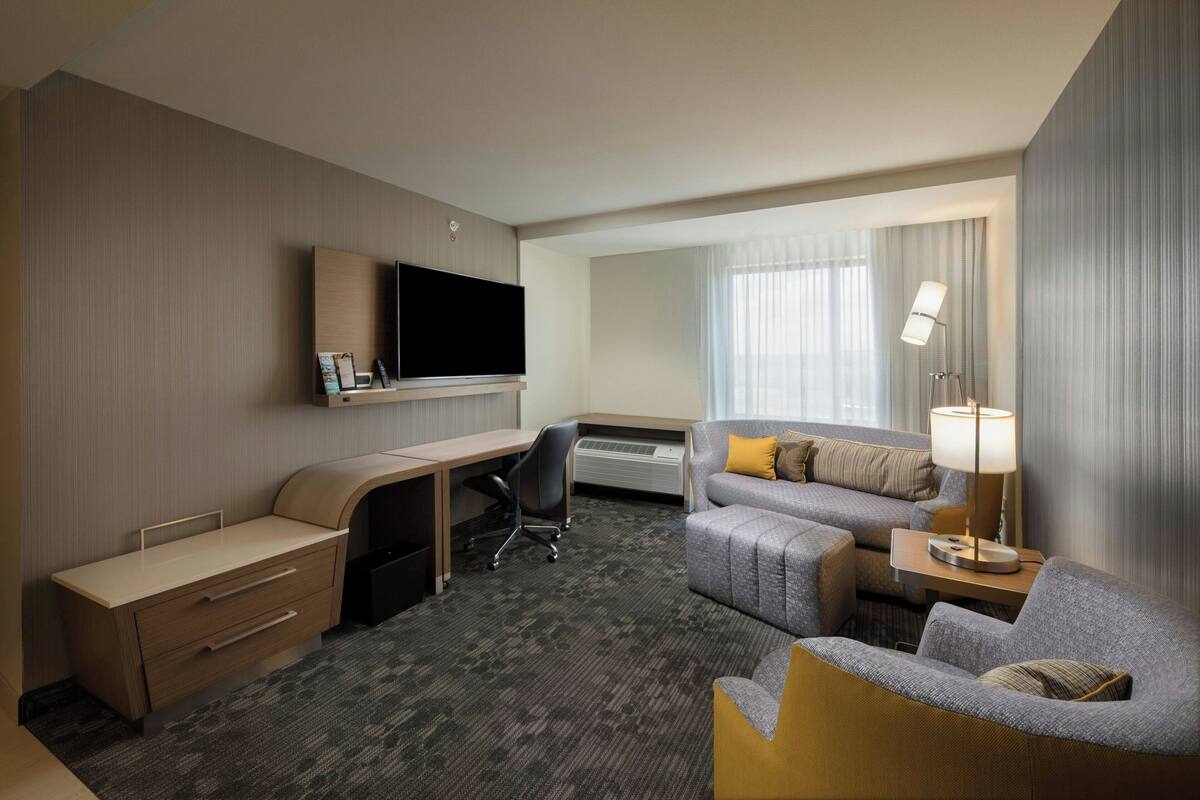 Ein Hotelzimmer mit Schreibtisch, einer Couch, einem Fernseher und einer Lampe.