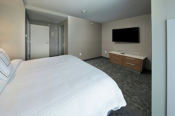 Una habitación de hotel con una cama grande, un televisor montado en la pared, un aparador de madera y una puerta que da a otra habitación.