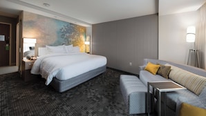 A hotel room with a large bed, a sofa, a small table, and a wall with a colorful mural. - Courtyard by Marriott Russellville (Russellville)