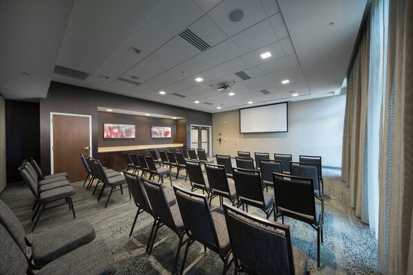 A conference room with rows of chairs, a projector screen, and a presentation area.