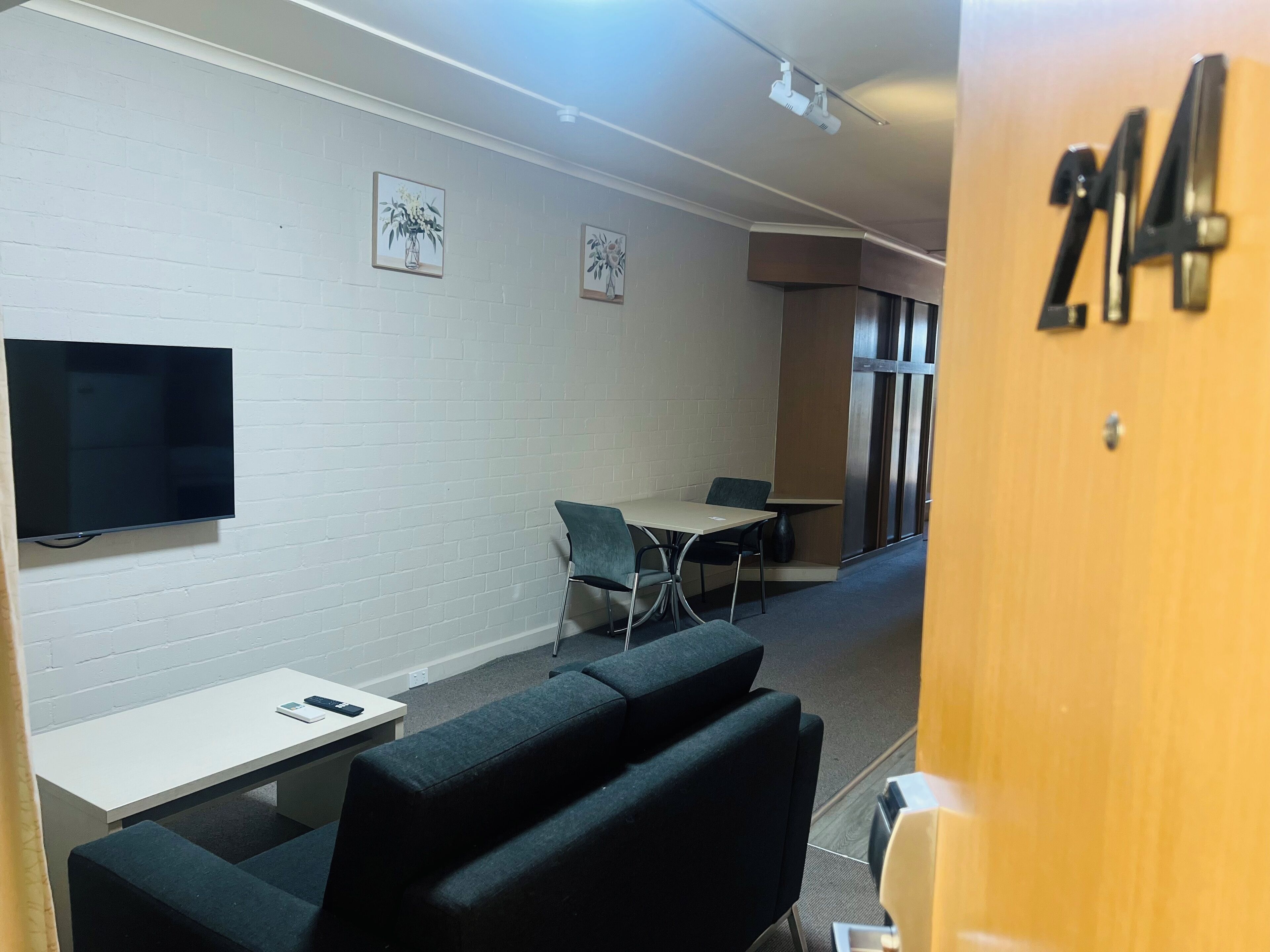Een moderne vergaderruimte met een flatscreen televisie, een witte baksteenmuur, twee ingelijste bloemwerken, een bank en een tafel met stoelen.