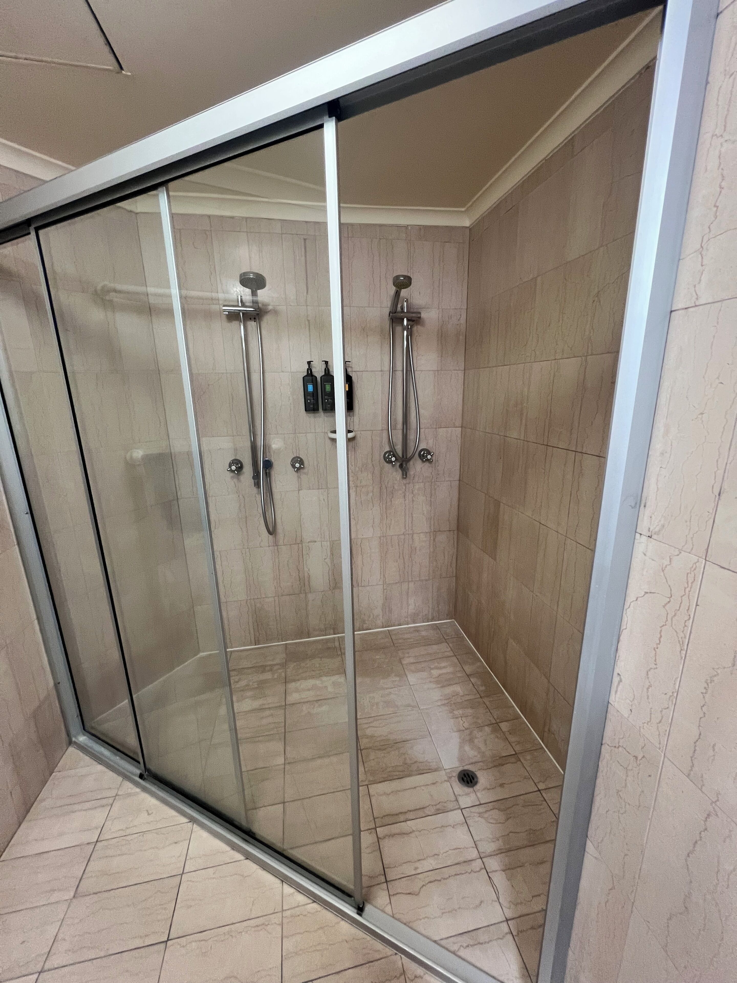 A glass-enclosed shower area with a control panel and handheld showerheads.