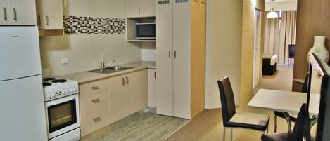 A compact kitchen with a stove, oven, microwave, and a small sink. There is a dining area with a table and chairs.