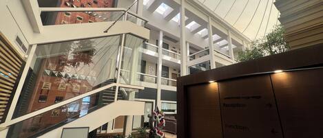 A multi-level atrium with a reception area, a staircase, and a view of a building with red brick walls and multiple windows.