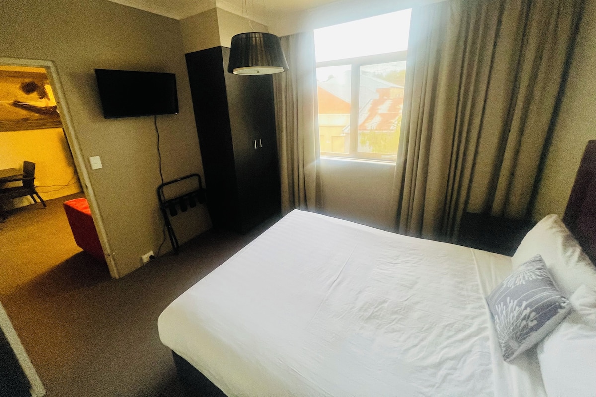 Ein Hotelzimmer mit Bett, Fernseher, Kleiderschrank und einem Fenster mit Vorhängen.