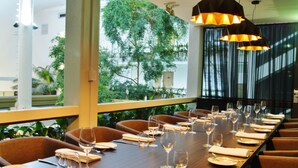 A dining area with a long table set for a meal, surrounded by chairs, with a view of greenery outside. - Pavilion Hotel Wagga Wagga (Wagga Wagga)