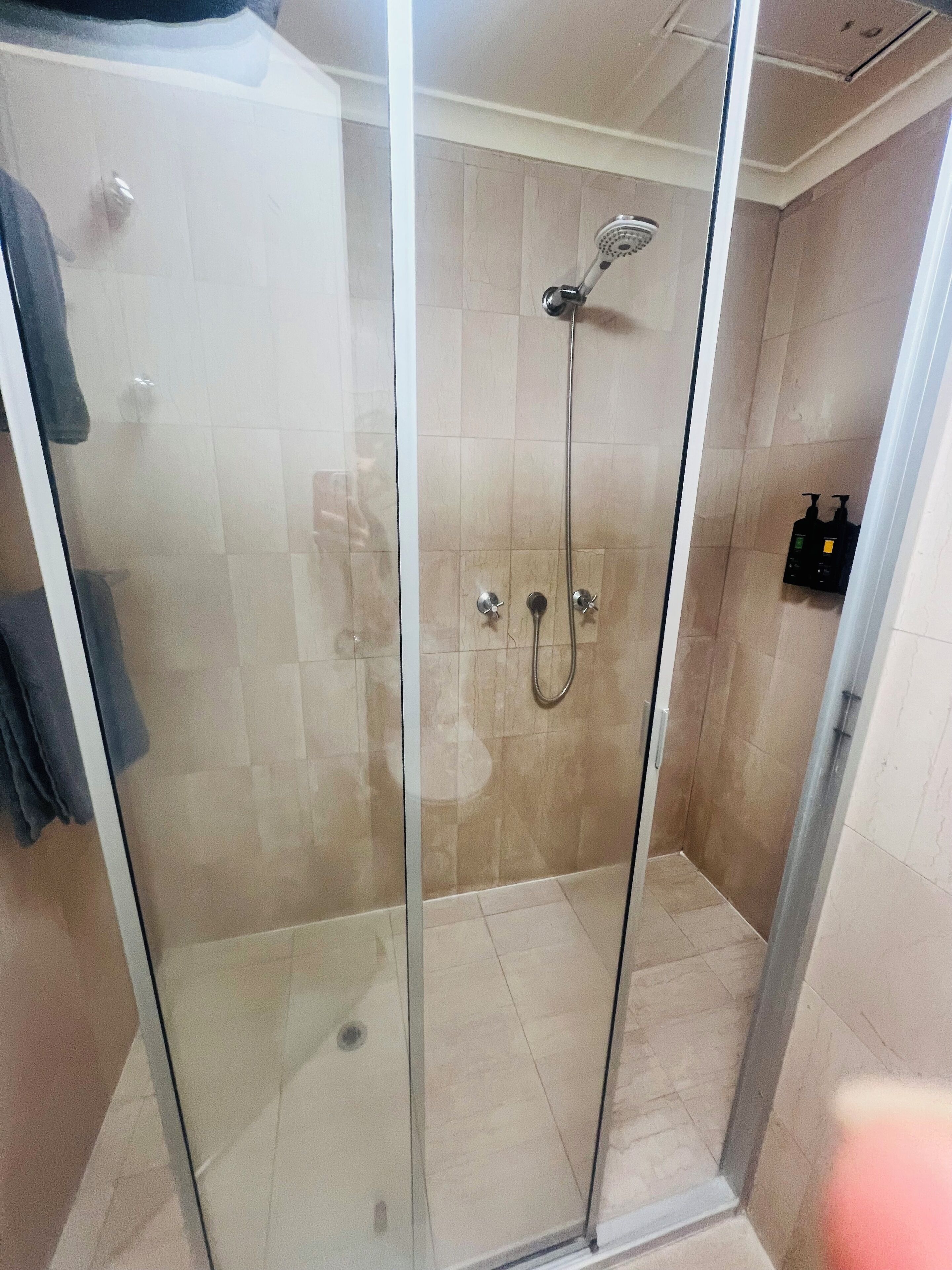 A glass-enclosed shower with a handheld showerhead and a wall-mounted faucet.