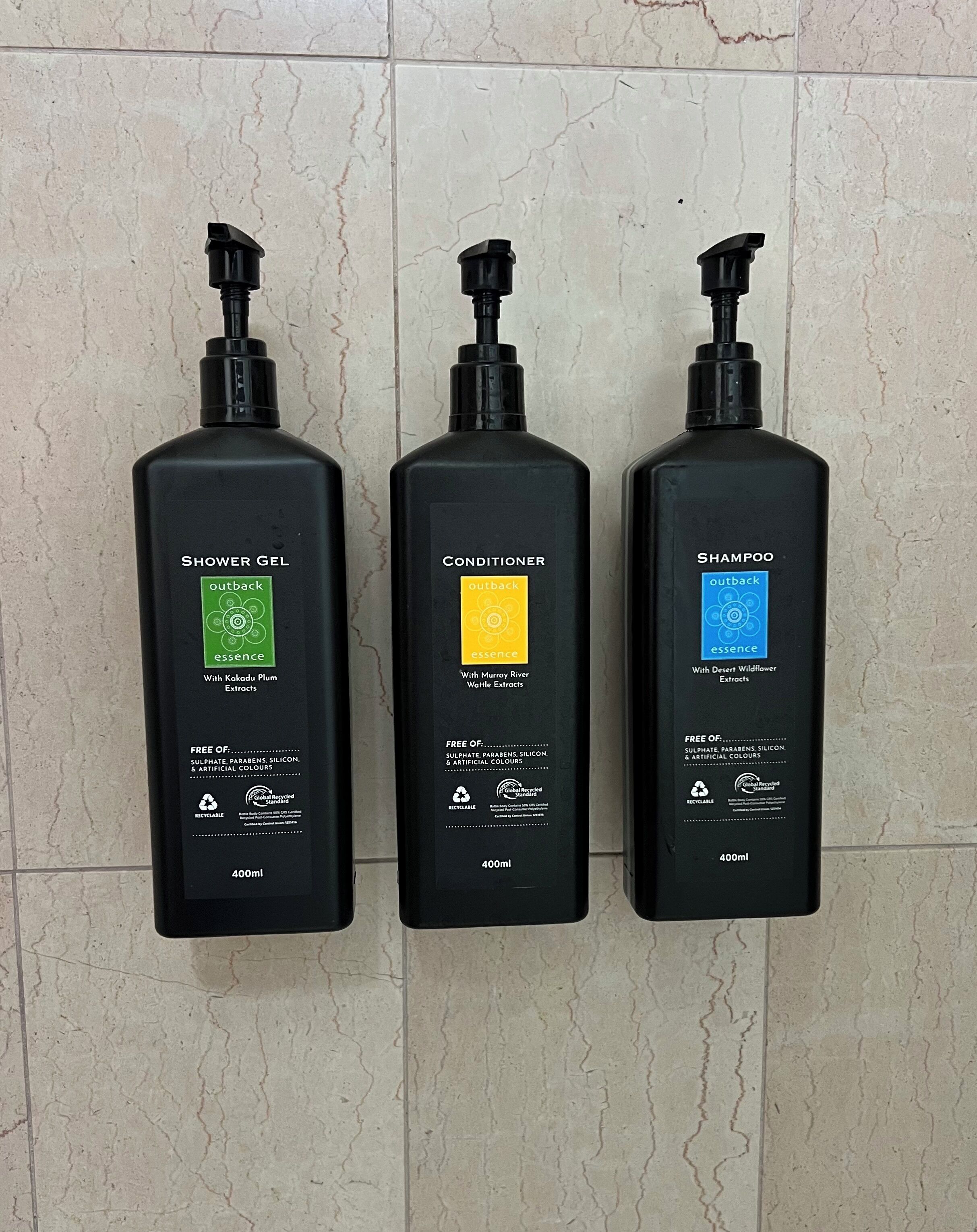 Three black bottles of Outback products on a tiled wall.