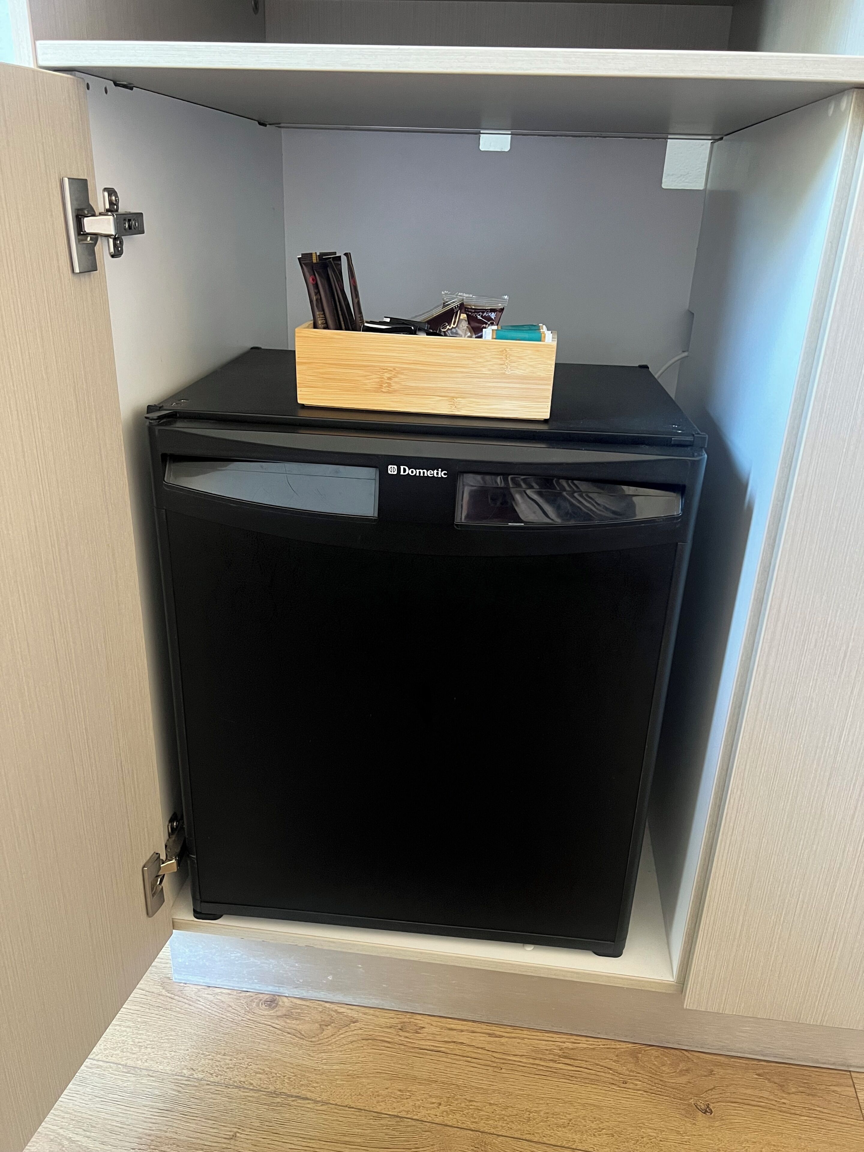 A black Domestic refrigerator in a kitchen cabinet with a wooden organizer on top.