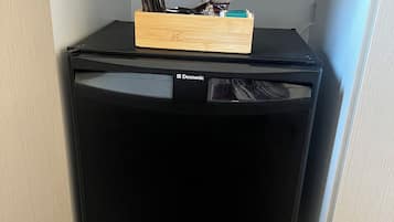 A black Domestic refrigerator in a kitchen cabinet with a wooden organizer on top.