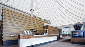 A modern reception area with a wooden panel wall, a reception desk, and a large screen displaying a room. - Pavilion Hotel Wagga Wagga (Wagga Wagga)