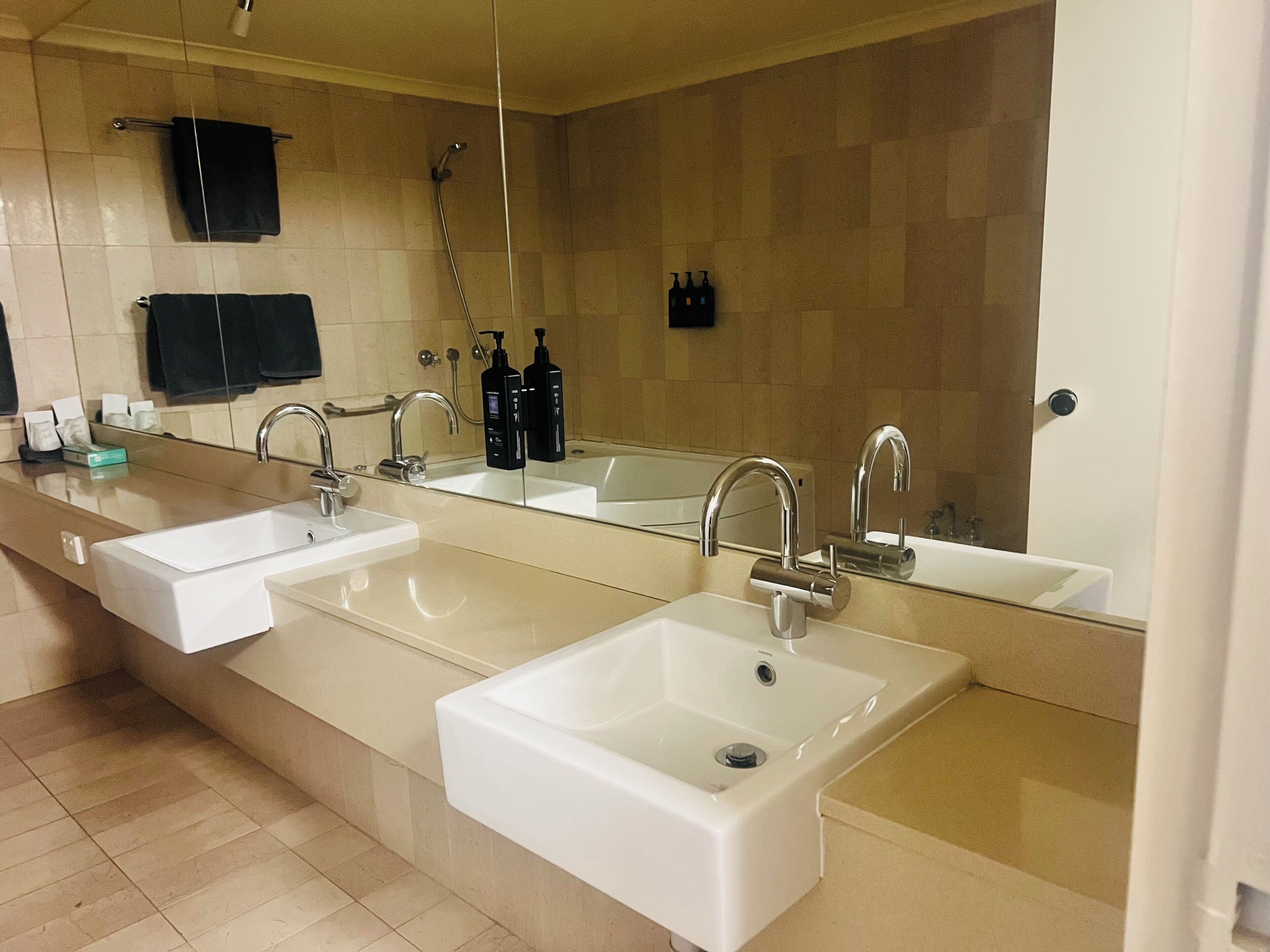 A modern bathroom with three sinks, a large mirror, and a shower area.