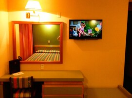Une chambre d’hôtel avec un lit, un téléviseur fixé au mur et une petite table avec une lampe.