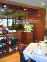L’intérieur d’un restaurant avec des lambris en bois, un meuble à vin et une table dressée pour deux personnes, agrémentée d’un vase de fleurs.