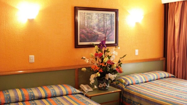 A hotel room with two beds, a small table with a vase of flowers, a painting on the wall, and a telephone on the table. - Segovia Regency Hotel (Mexico City)