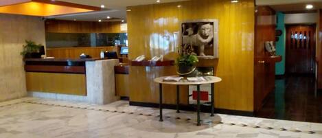 Vestíbulo de hotel con mostrador de recepción, suelo de mármol y una gran escultura en la pared.