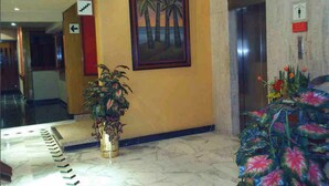 A lobby with a marble floor, a framed painting of palm trees, a potted plant, and a floral arrangement. - Segovia Regency Hotel (Mexico City)