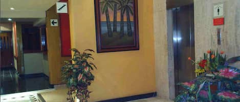 A lobby with a marble floor, a framed painting of palm trees, a potted plant, and a floral arrangement.