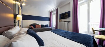 A hotel room with two beds, a TV, a radiator, and a window with curtains.