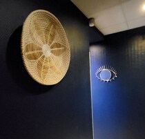 A wall with a woven fan and a circular metal fixture.