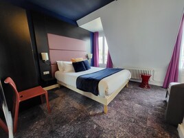 Una camera d'albergo moderna con un letto, un comodino, una sedia rossa e una finestra con tende.