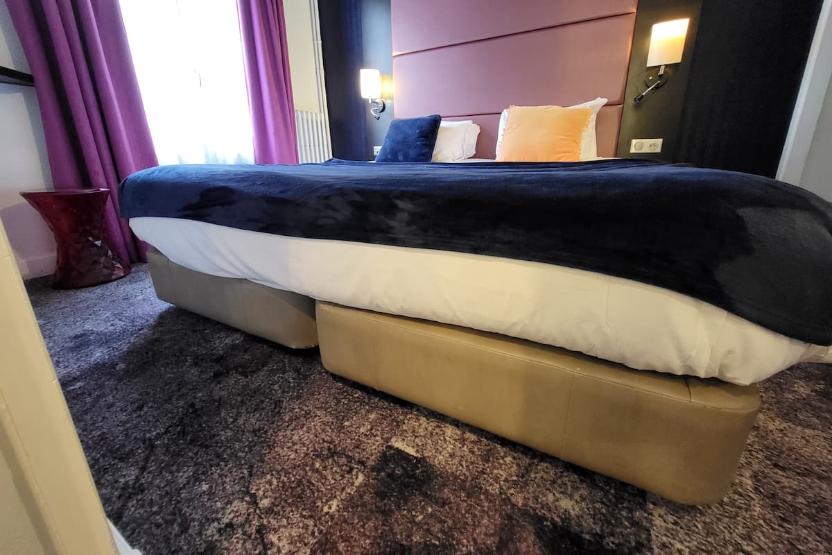 Une chambre d’hôtel avec un grand lit, une tête de lit, une table de chevet et une lampe fixée au mur.