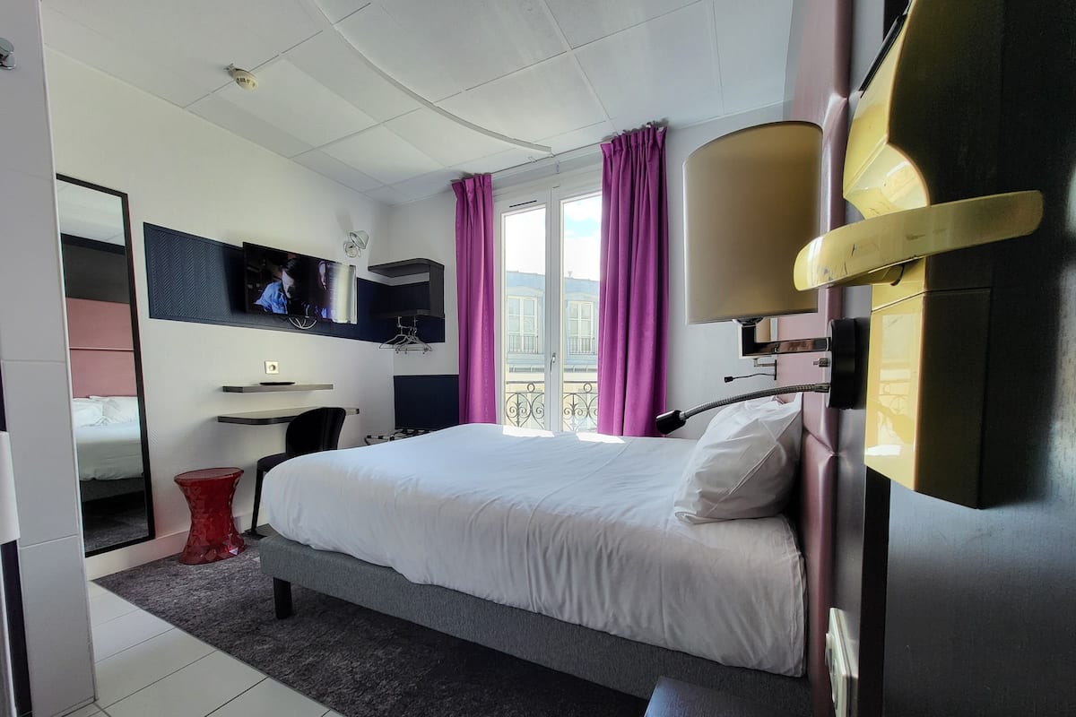 Une chambre d’hôtel avec un lit, une télévision, un bureau et un balcon avec des rideaux.