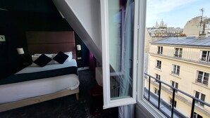 A hotel room with a bed, a window, and a view of city buildings.