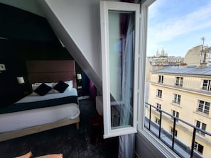 Un cuarto de hotel con cama, ventana y vistas a edificios de la ciudad.
