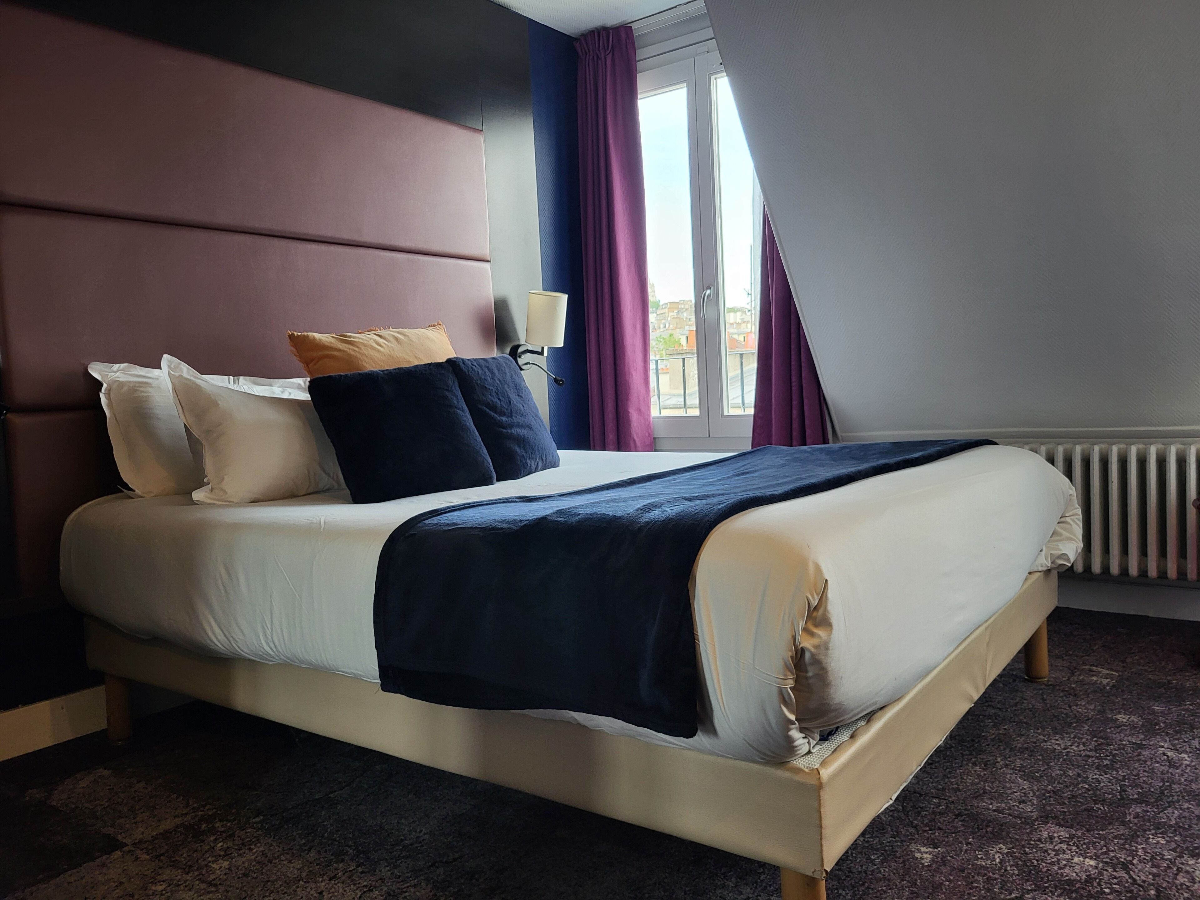 Una cama con cabecera, almohadas, una colcha y una ventana con cortinas.