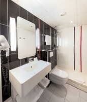 A modern bathroom with a white sink, mirror, and toilet, black and white tiled walls, and a shower area with red and blue stripes.