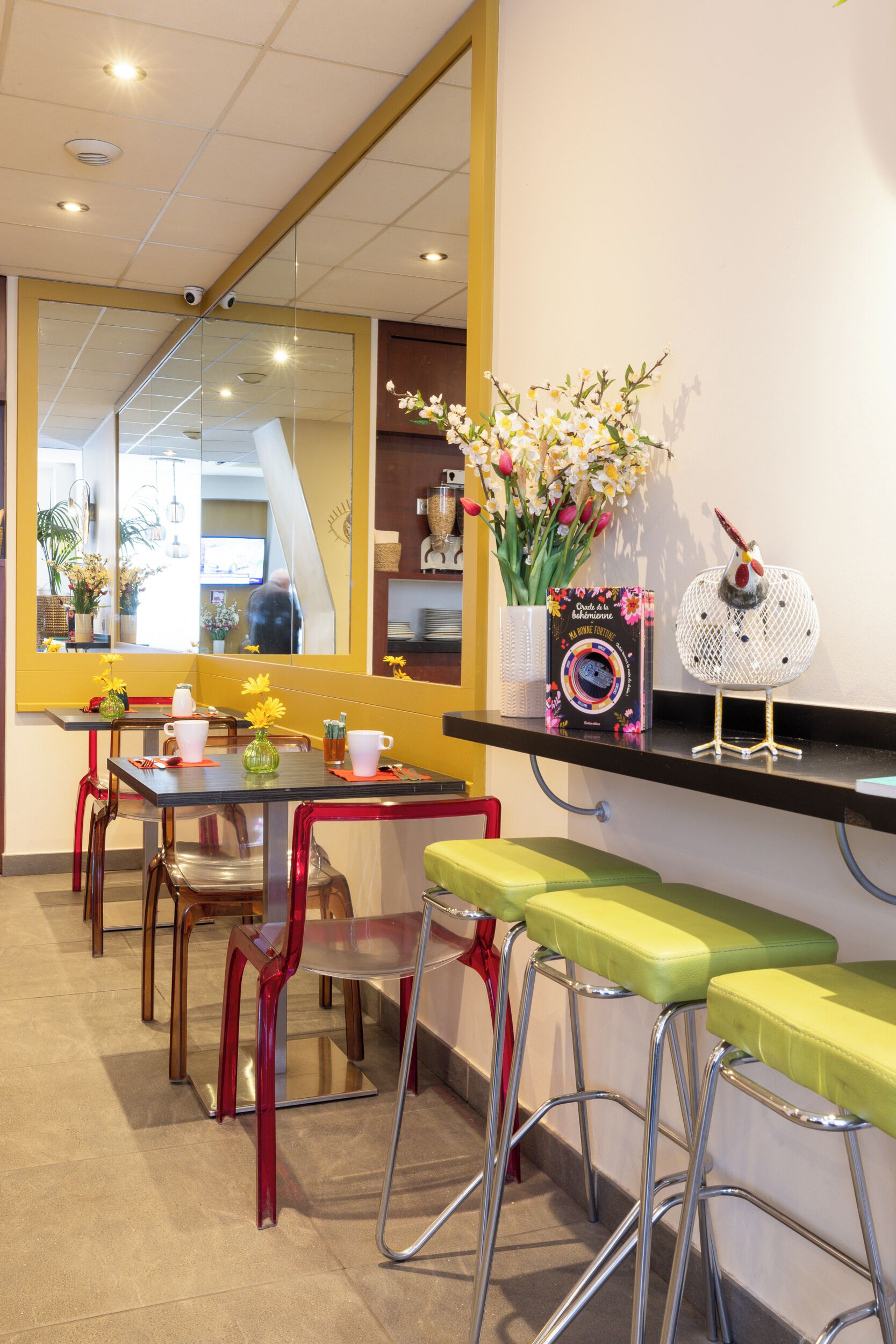 Un restaurante con una decoración en tonos amarillo y blanco, que cuenta con una barra larga con taburetes, un espejo grande y una escultura decorativa de un pájaro.