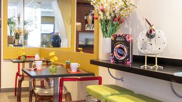 Un restaurante con una decoración en tonos amarillo y blanco, que cuenta con una barra larga con taburetes, un espejo grande y una escultura decorativa de un pájaro.