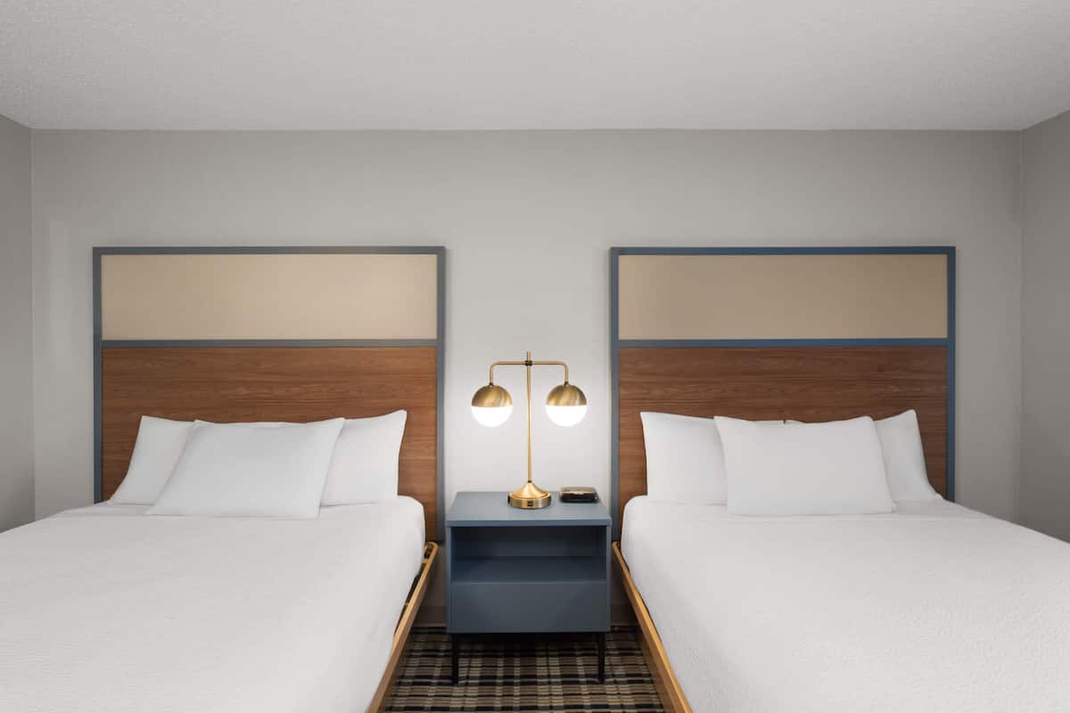 A hotel room with two beds, a nightstand with a lamp, and a check-in counter.