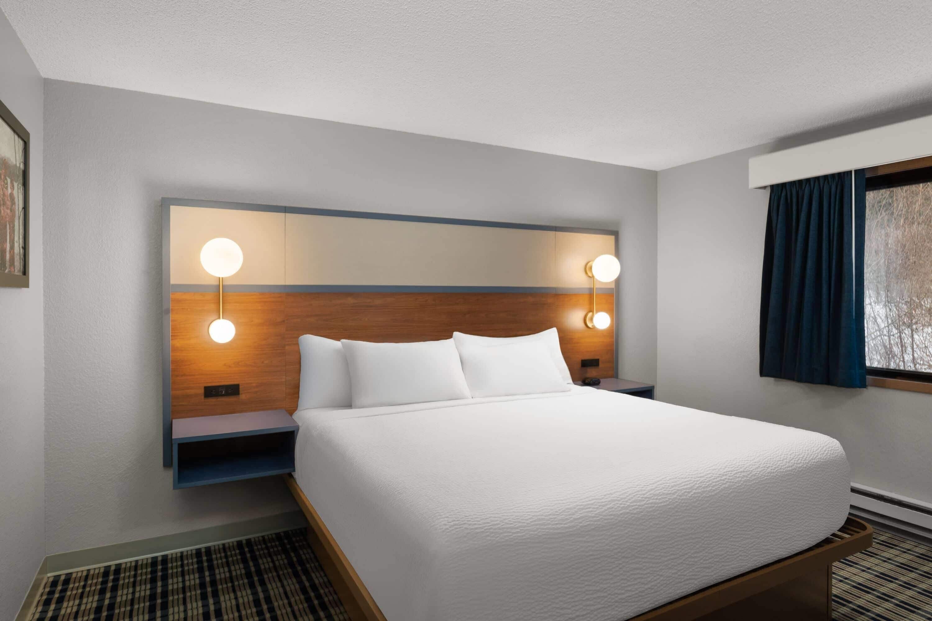 Une chambre d’hôtel avec un grand lit, deux tables de chevet, un luminaire fixé au mur et une fenêtre avec des rideaux.