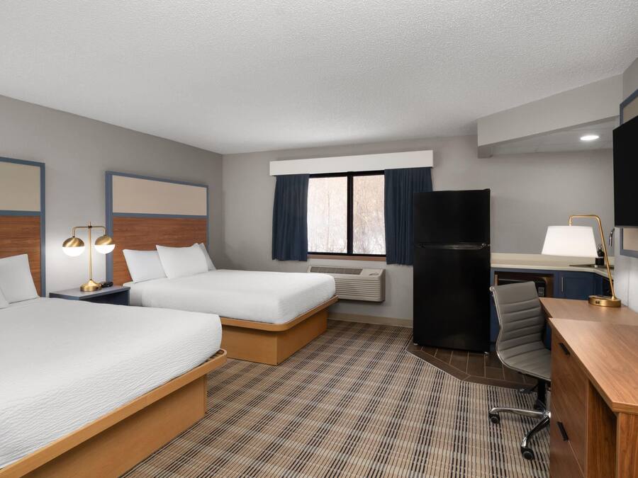 A hotel room with two beds, a desk, a chair, a TV, and a refrigerator.