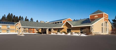 A hotel with a spacious parking lot, a covered outdoor area, and a building with a sloped roof featuring solar panels.