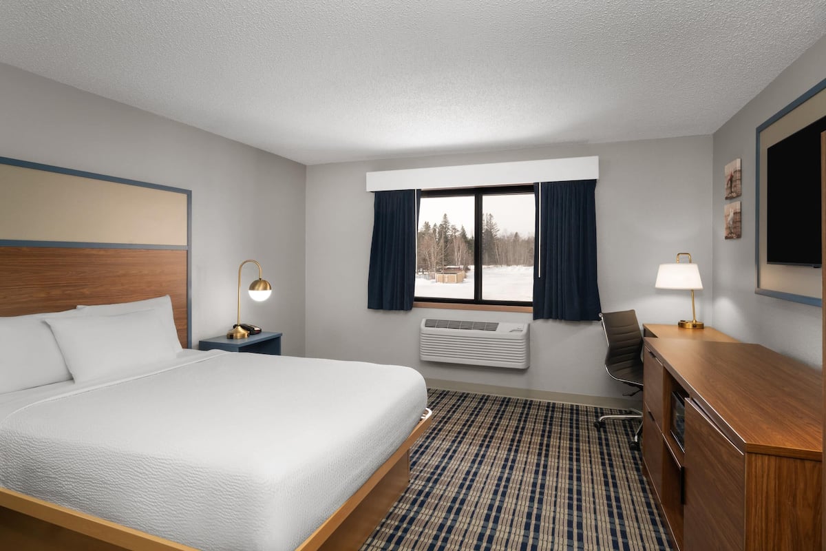 A hotel room with a large bed, a desk, a chair, a window with curtains, and a wall-mounted TV.