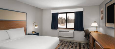 Een hotelkamer met een groot bed, een bureau, een stoel, een raam met gordijnen en een aan de muur bevestigde televisie.