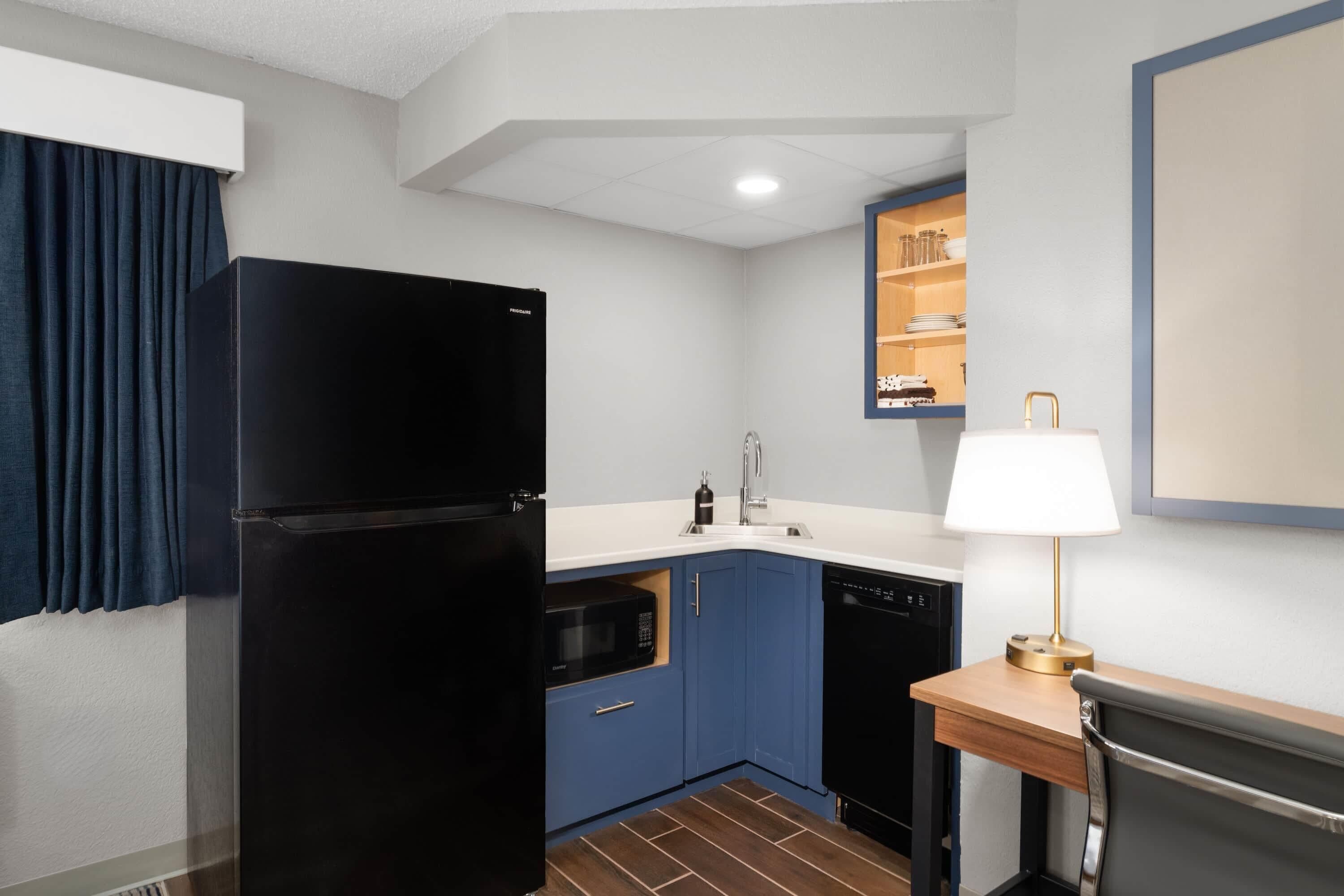 A compact kitchen with a black refrigerator, blue cabinets, a microwave, and a dishwasher.