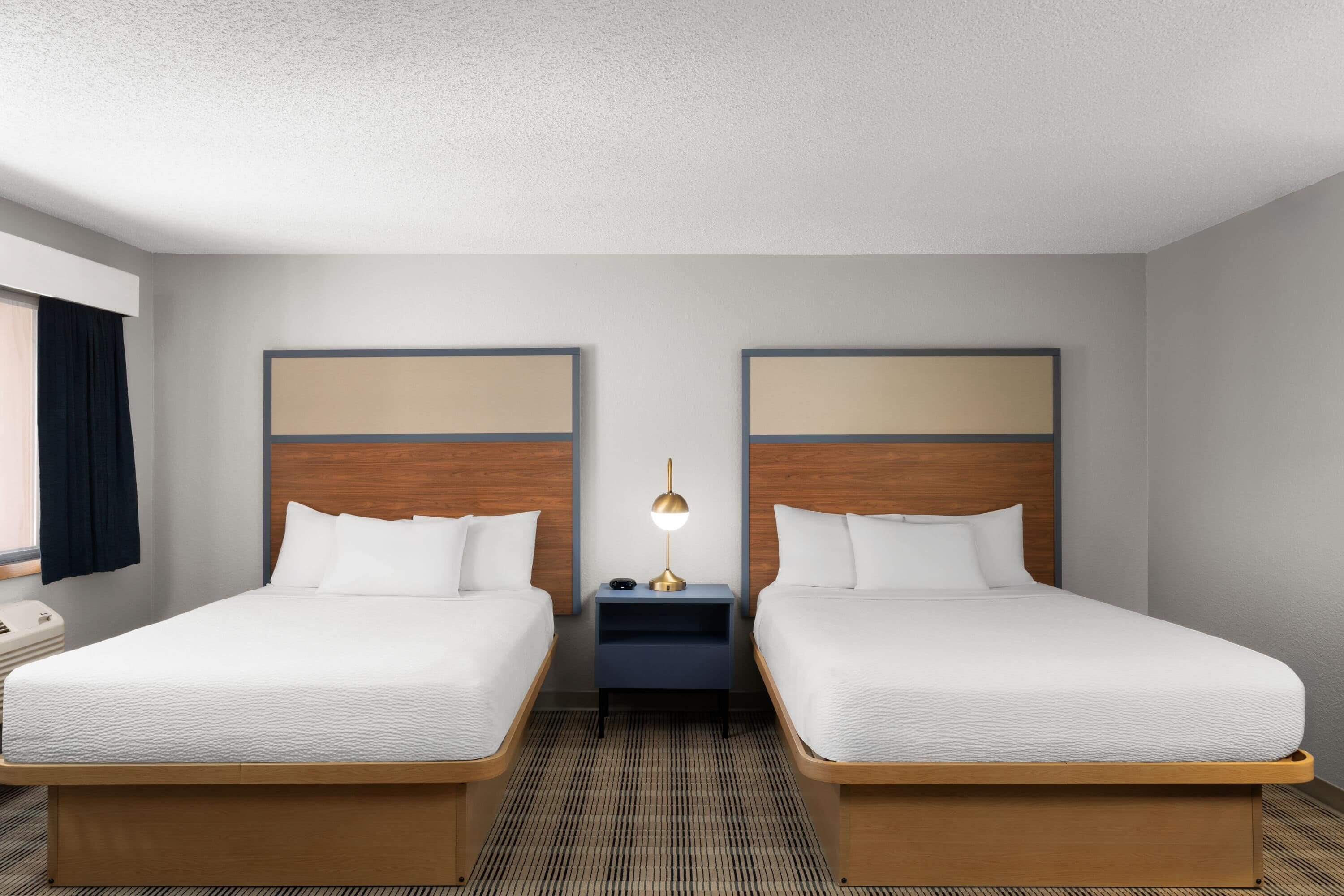 Une chambre d’hôtel avec deux lits simples, une table de chevet avec une lampe et une fenêtre avec des rideaux.