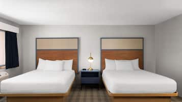 Une chambre d’hôtel avec deux lits simples, une table de chevet avec une lampe et une fenêtre avec des rideaux.