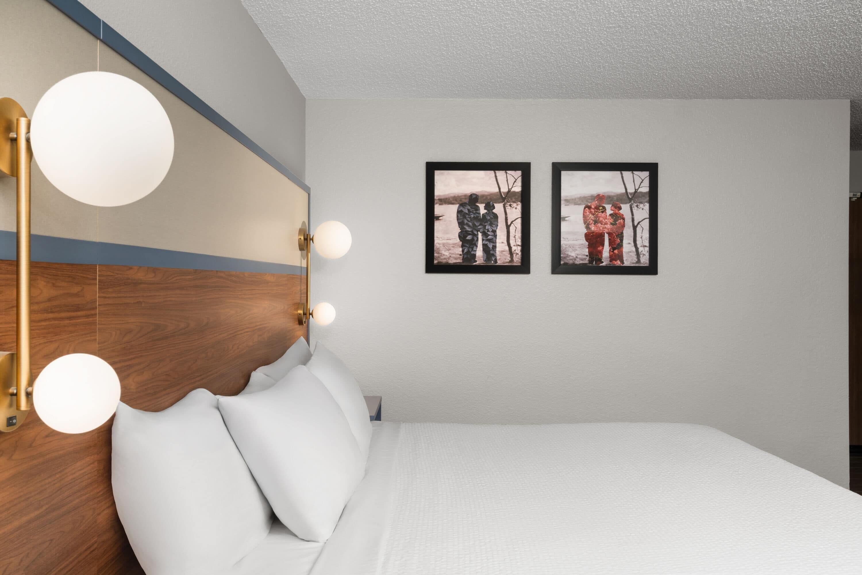 A modern hotel room with a large bed, a wooden headboard, and two framed photographs on the wall.