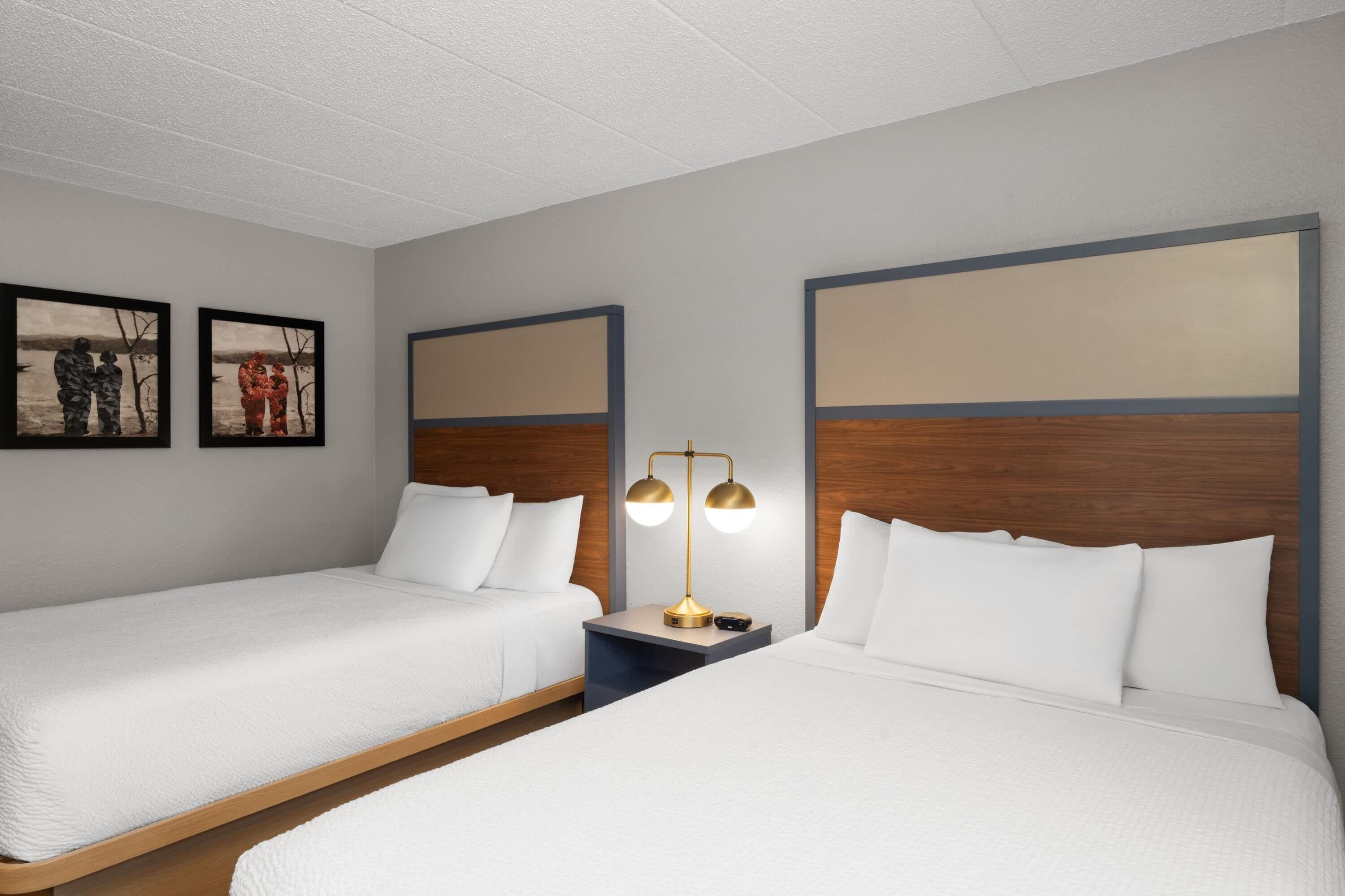 Ein Hotelzimmer mit zwei Einzelbetten, einem Nachttisch mit Lampe und zwei gerahmten Bildern an der Wand.