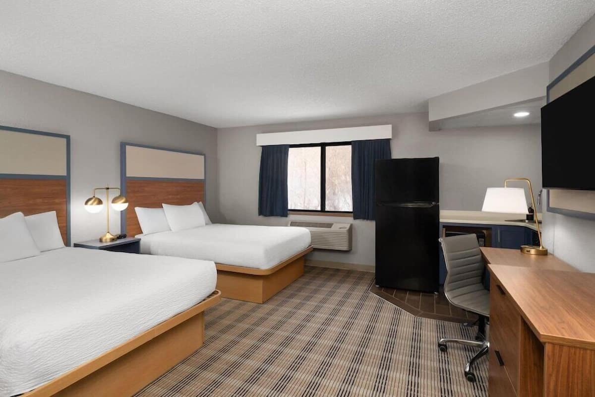A hotel room with two beds, a desk, a chair, a TV, and a window with curtains.