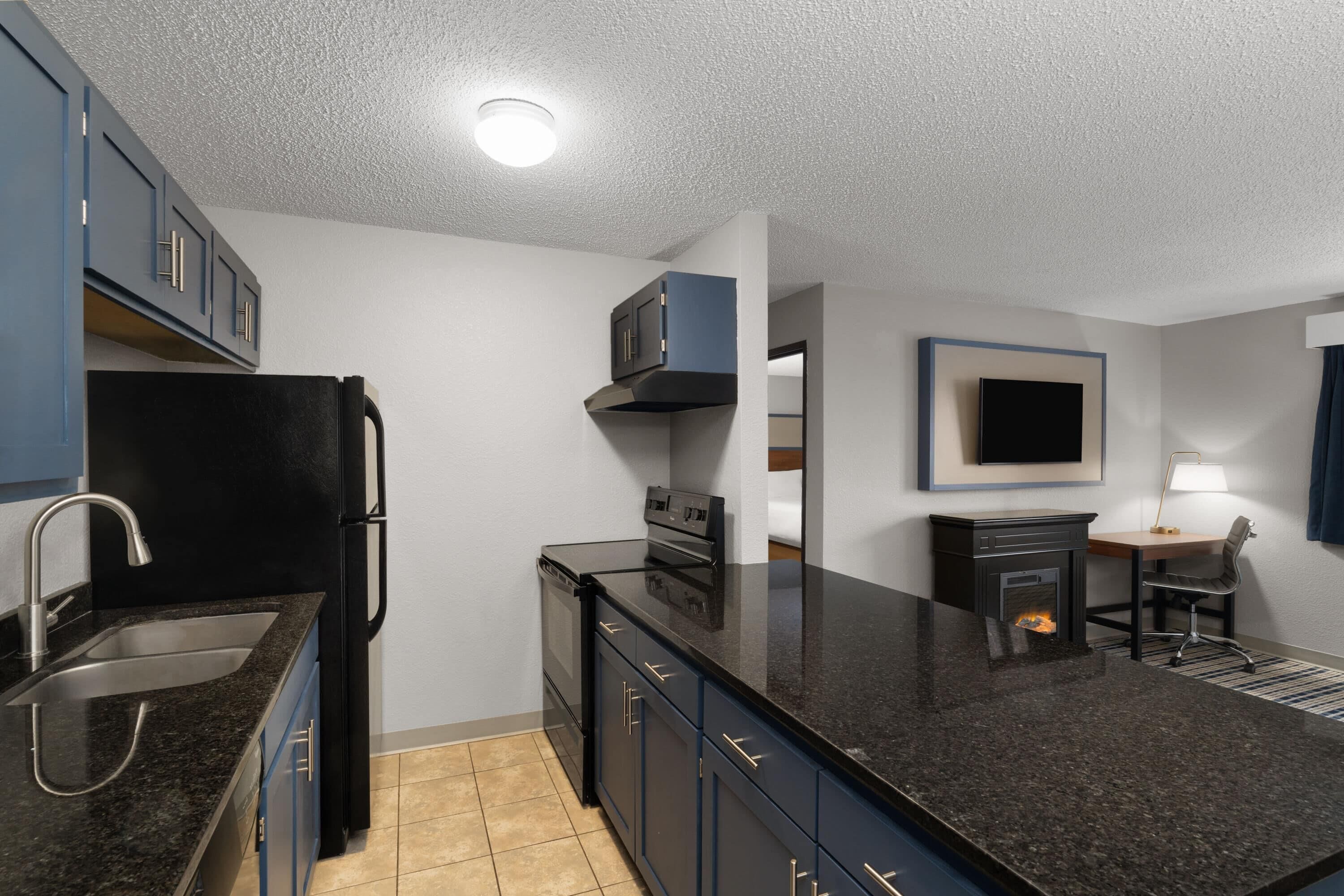 A modern kitchen with a black refrigerator, stainless steel sink, and dark blue cabinets.