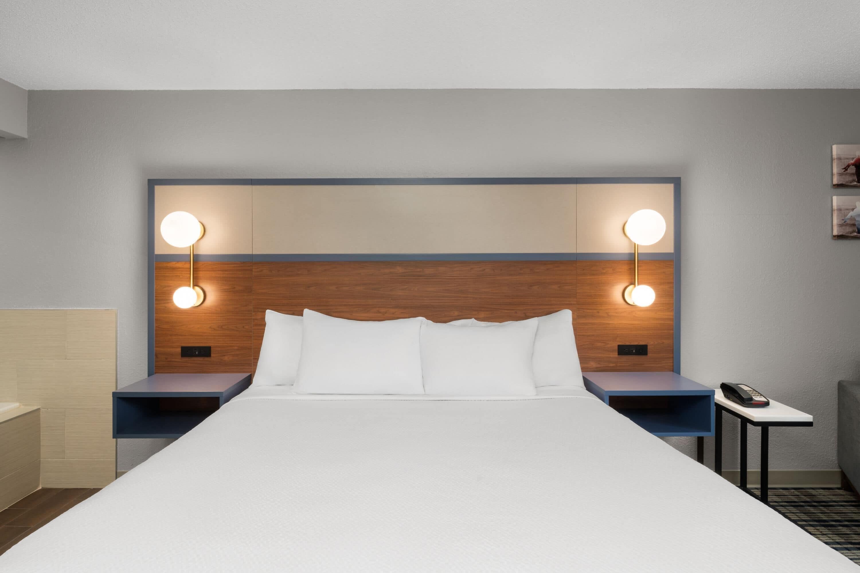 A hotel room with a large bed, two bedside tables with lamps, a small table with a phone, and a headboard with built-in lighting.