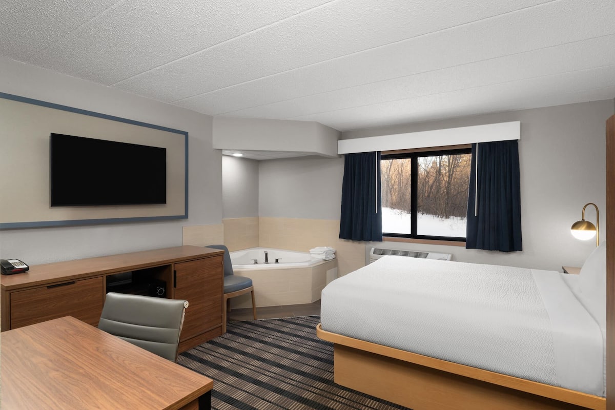 A hotel room with a bed, desk, chair, and a large window with curtains.